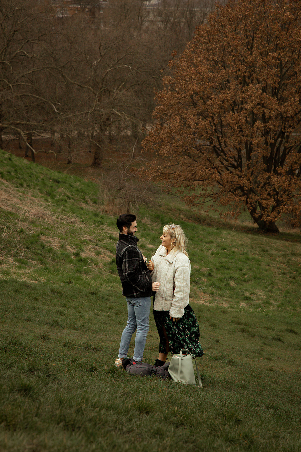 Couple standing together after just getting engaged, laughing with each other in Greenwich park, London.