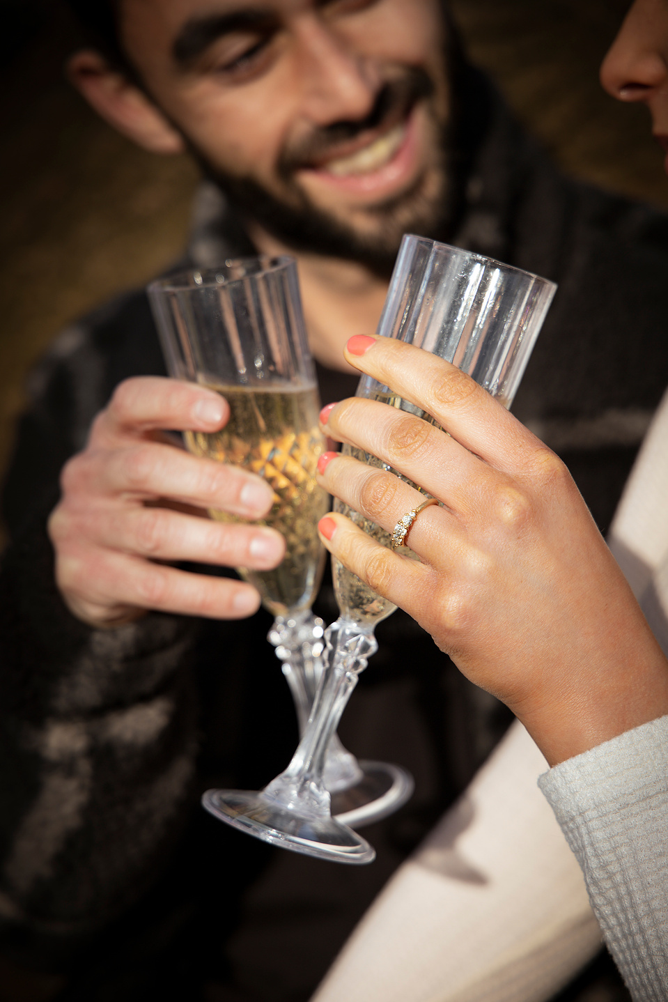 Couple smiling and having a glass of champagne after just getting engaged. Her ring is glistening in the sunlight