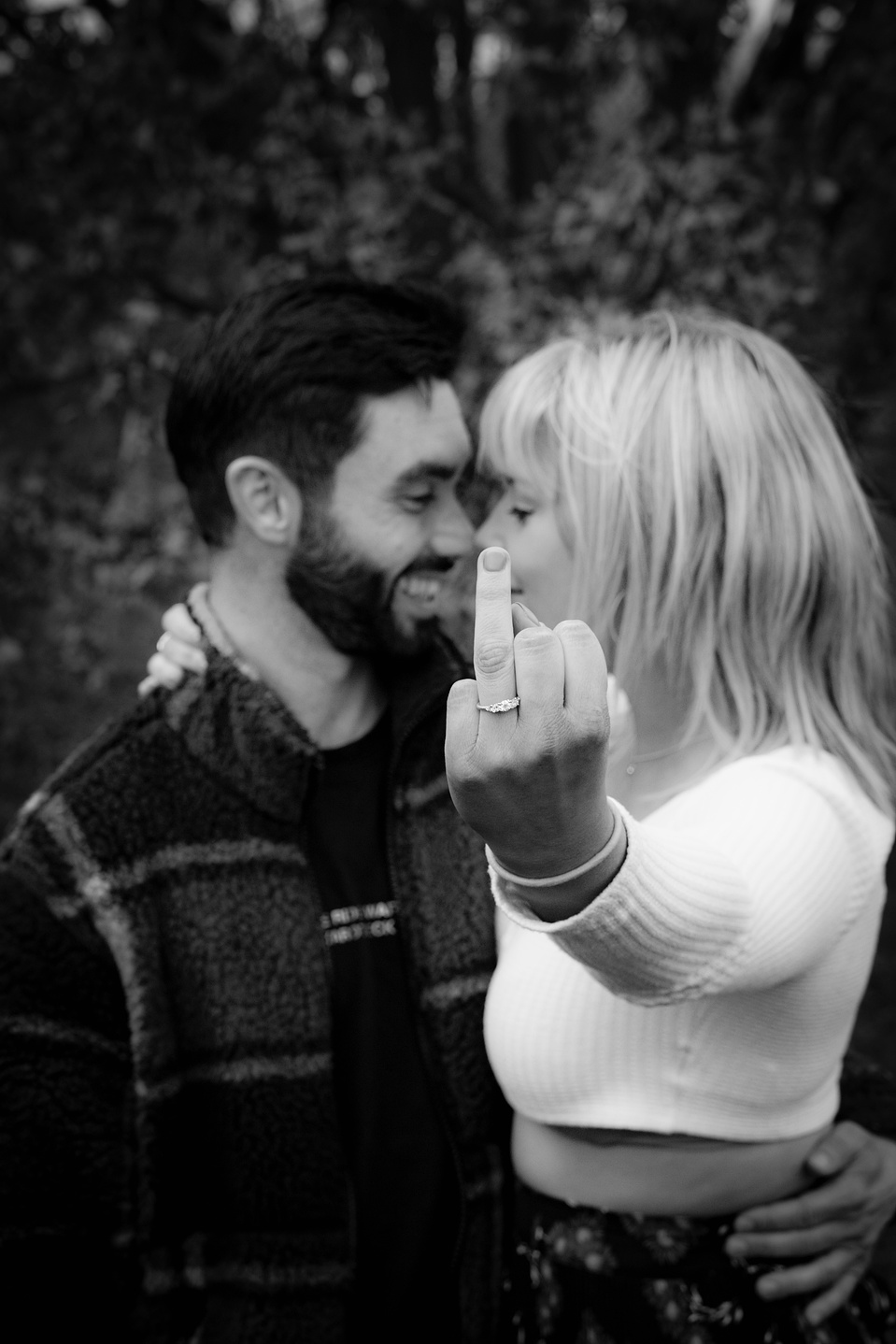 Couple embracing and looking at each other after just getting engaged. Her holding up her finger ring to show off her new ring.