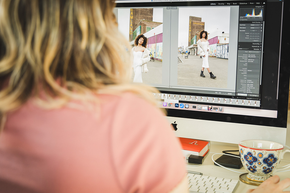Woman sitting at her desk editing photos in Lightroom with a mug and book on her desk at home