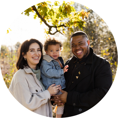 Couple standing on a sunny day under a tree with their son all smiling in to the camera in woodland near Ashford in Kent