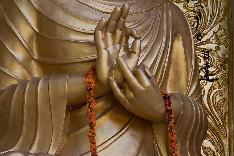 Buddha's hands holding orange garland.