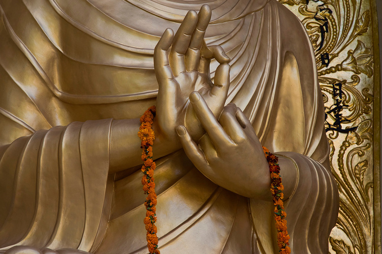 Buddha's hands holding orange garland.