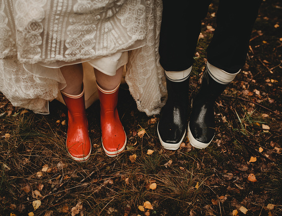 Bei einer Regenhochzeit in Brandenburg im Herbst steht das Brautpaar in Gummistiefeln für besondere Hochzeitsfotos im Wald.