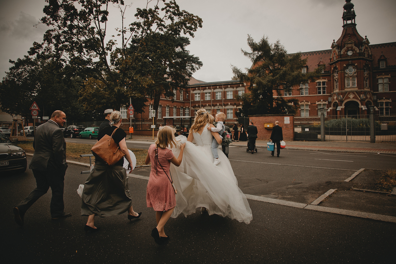 Braut rennt in Berlin über eine Straße während das Blumenmädchen ihre Schleppe trägt