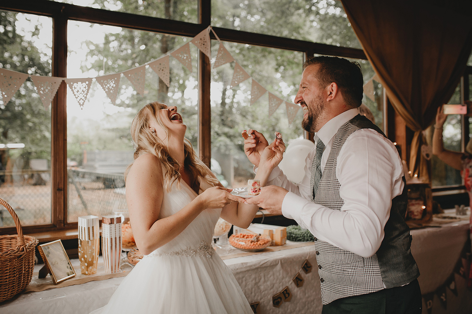 Braut lacht während der Bräutigam sie mit der Hochzeitstorte füttert