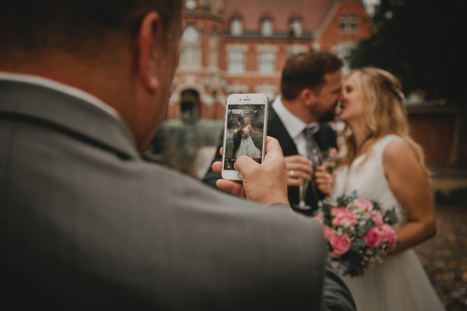 Hochzeitsgast macht mit dem Smartphone ein Foto von einem sich küssenden Brautpaar