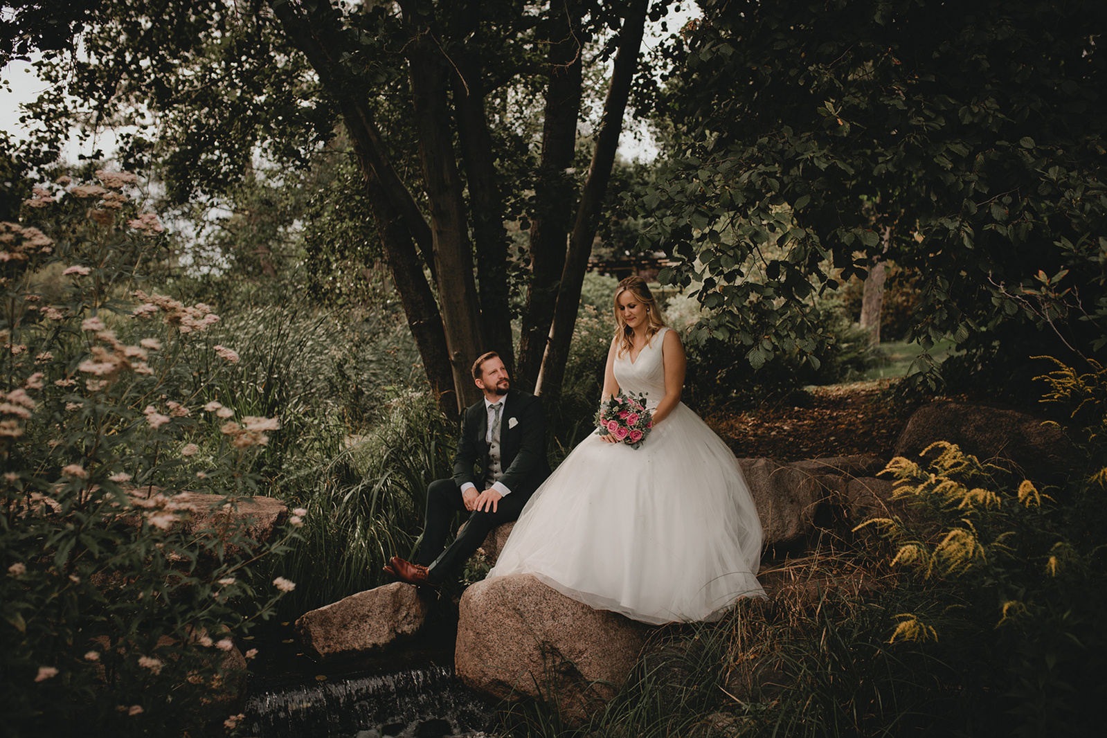 Brautpaar sitzt auf Steinen am Bach im Britzer Garten
