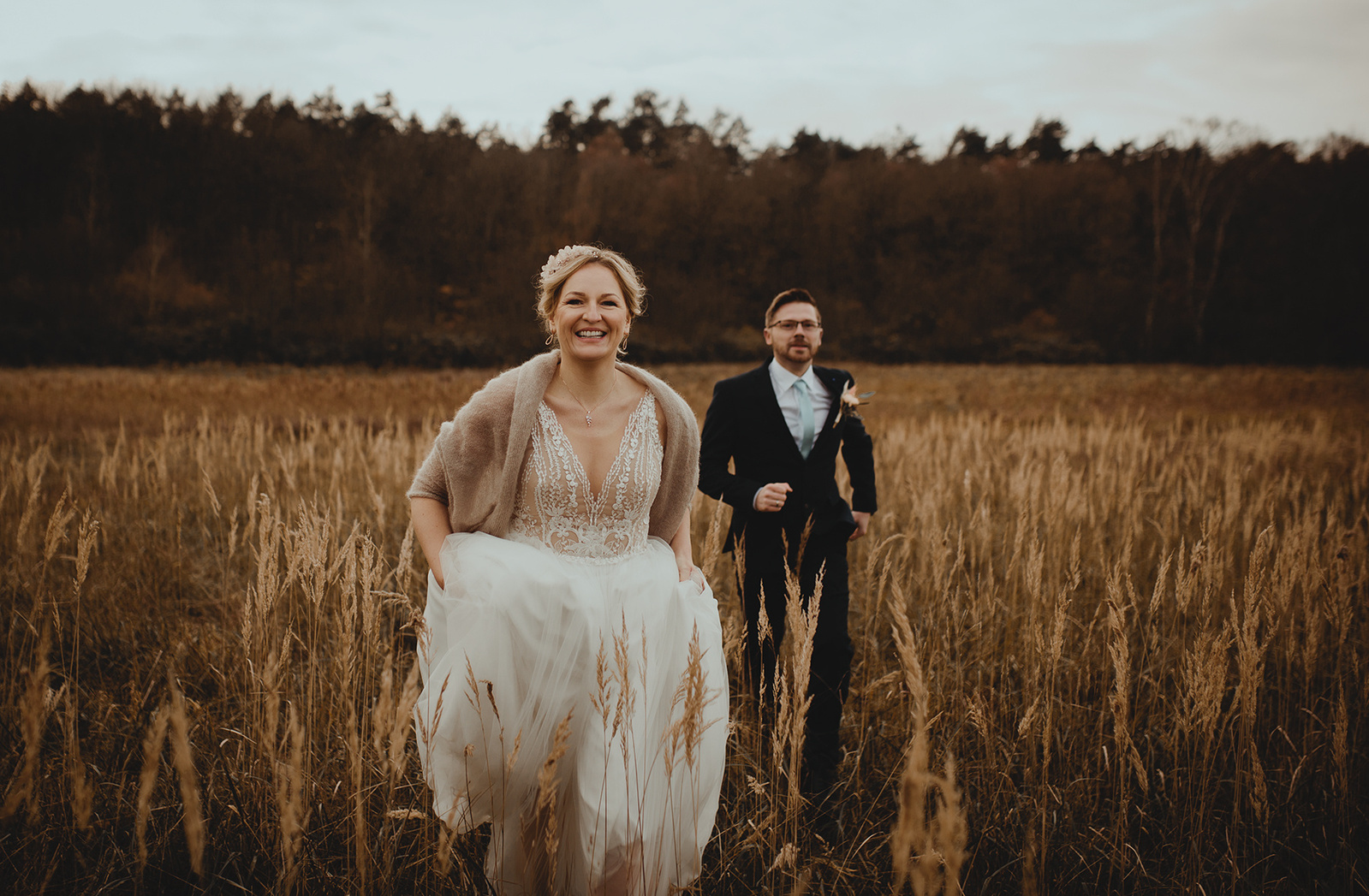 Lachendes Brautpaar rennt übers Feld für Hochzeitsfotos in Brandenburg