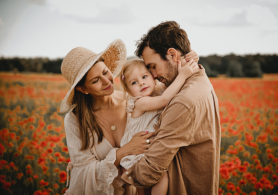 Eine junge Familie kuschelt beim Fotoshooting im Mohnfeld eng umschlungen miteinander. 