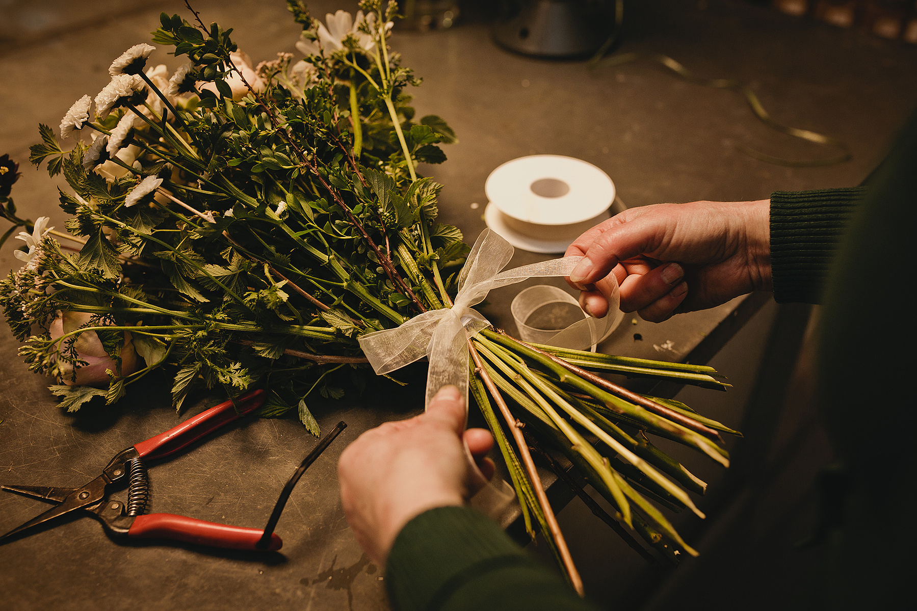 Detailaufnahme einer Businessreportage in Berlin. Eine Floristin bindet eine Schleife um einen Blumenstrauß.