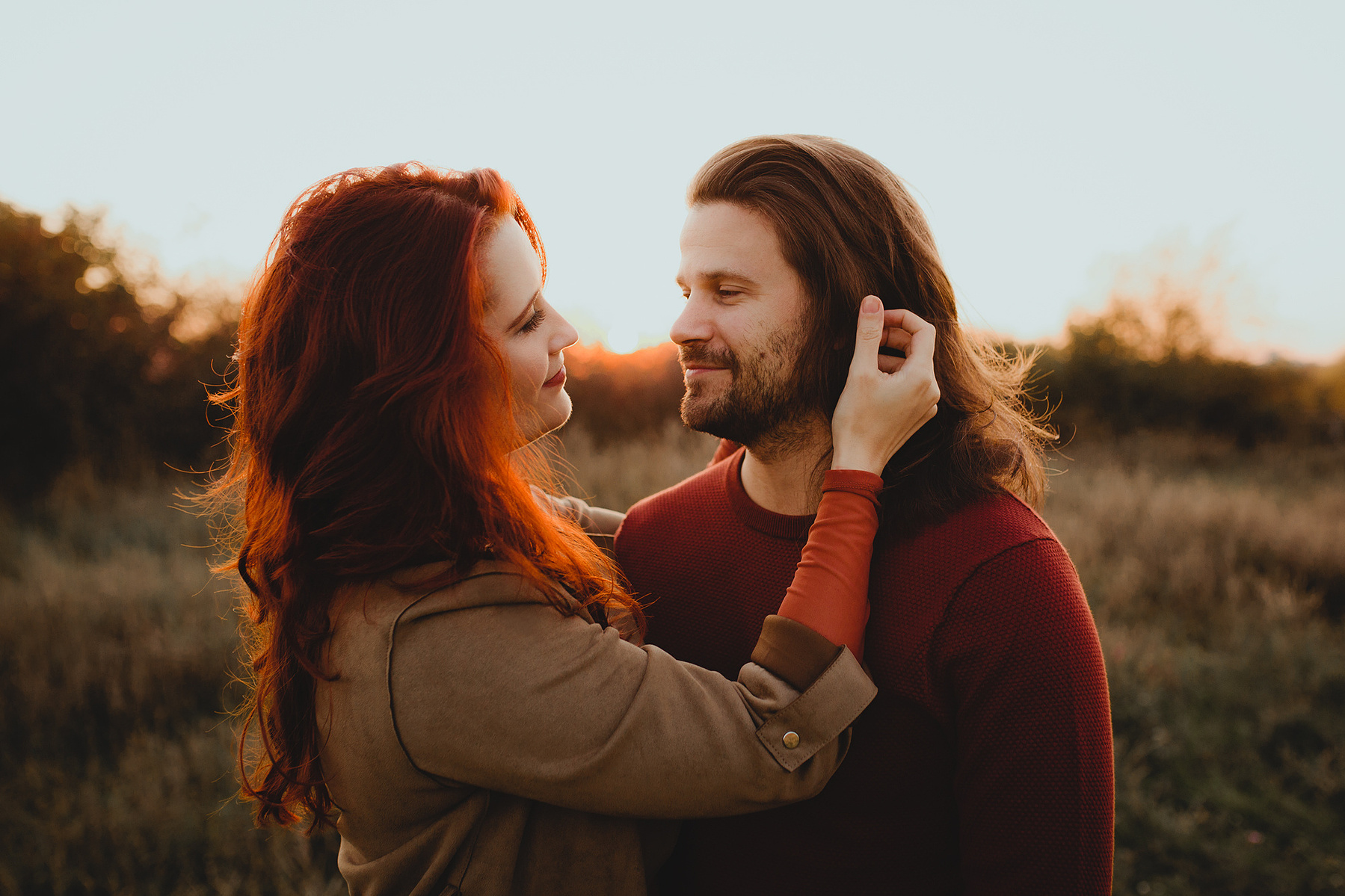 Authentisches Pärchen Fotoshooting im Abendlicht. In einem ungestellten Moment streicht sie ihm die langen Haare aus dem Gesicht.
