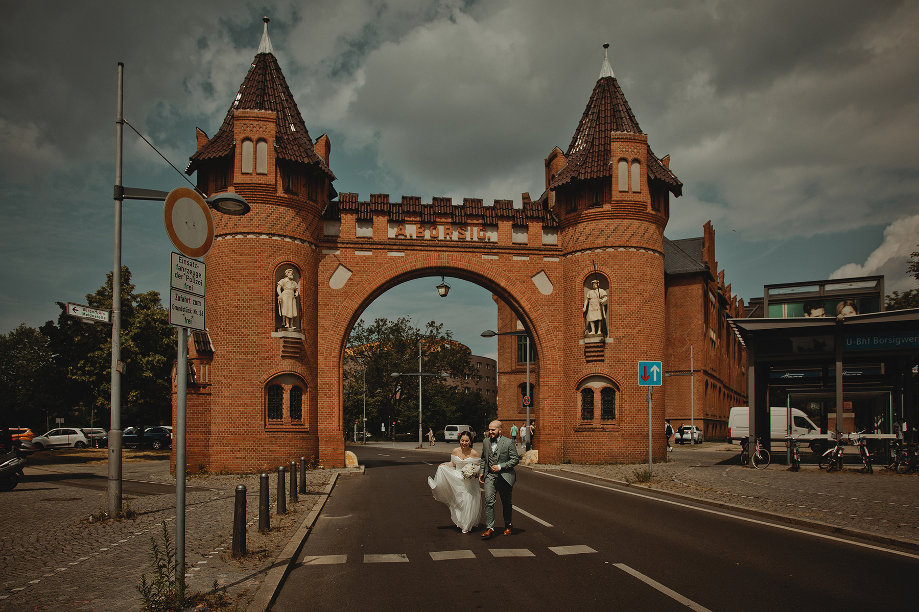 Vor dem historischen Borsigtor in Berlin-Tegel rennt ein Brautpaar für ungestellte Hochzeitsfotos über die Straße.