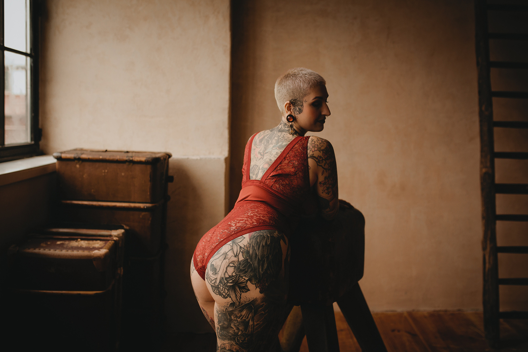 Eine tätowierte Frau stützt sich beim Boudoirshooting im Fotostudio in Berlin auf einen Hocker und dreht ihren Po zur Kamera.