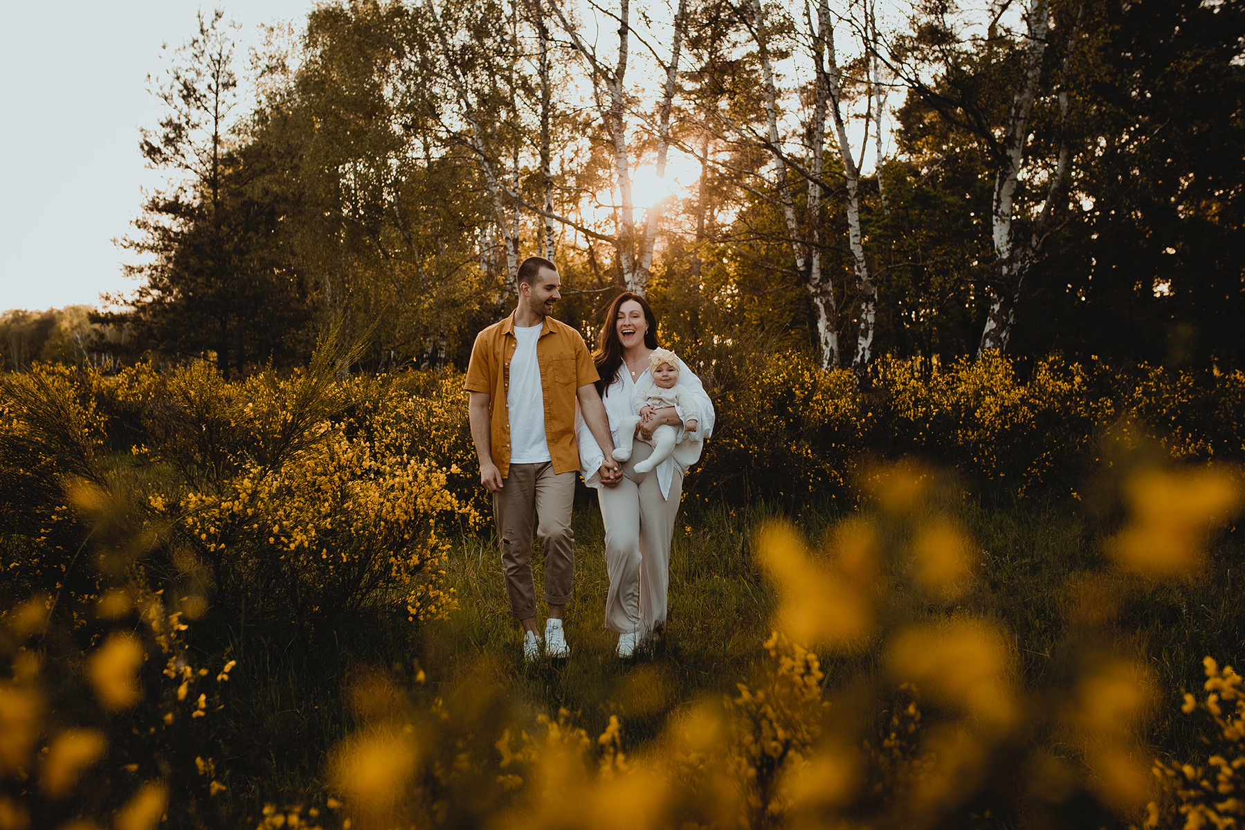 Beim Fotoshooting in der Natur läuft eine Familie in farblich passenden Outfits über eine Lichtung mit gelbem Ginster. 