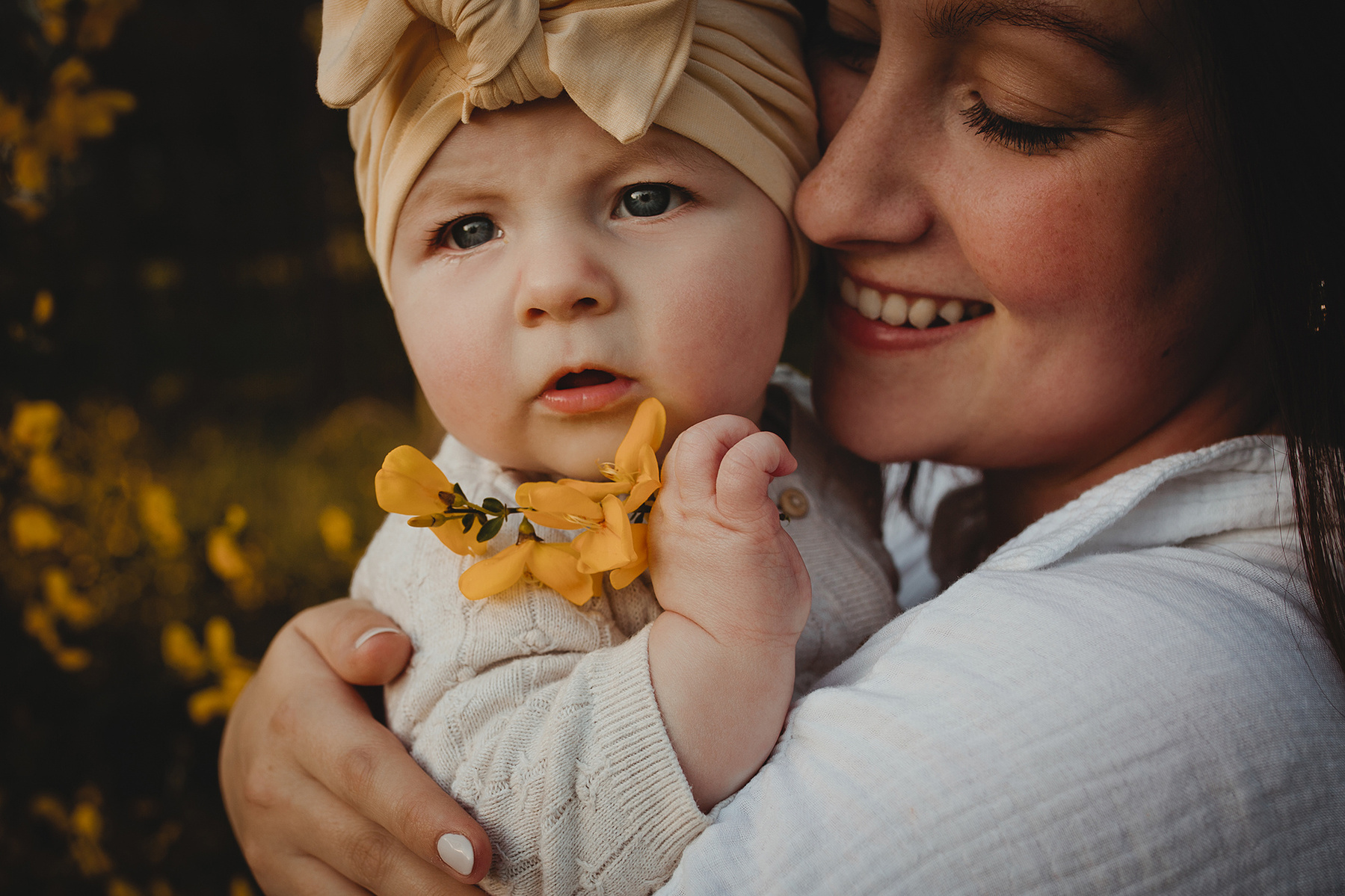 Ein kleines Mädchen mit einer Blume in der Hand wird von seiner Mutter beim Familien-Fotoshooting in der Natur liebkost.