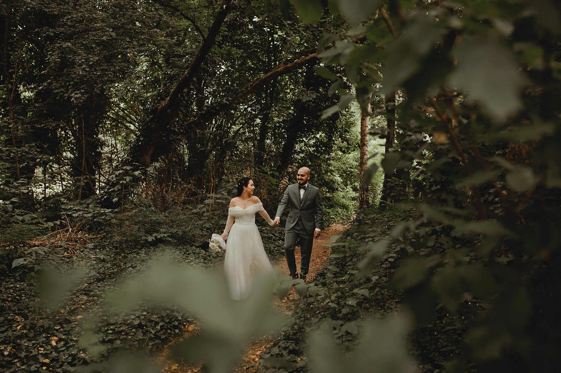 Ein Hochzeitspaar läuft beim Fotoshooting Hand in Hand auf einem kleinen Pfad durch einen Wald. 