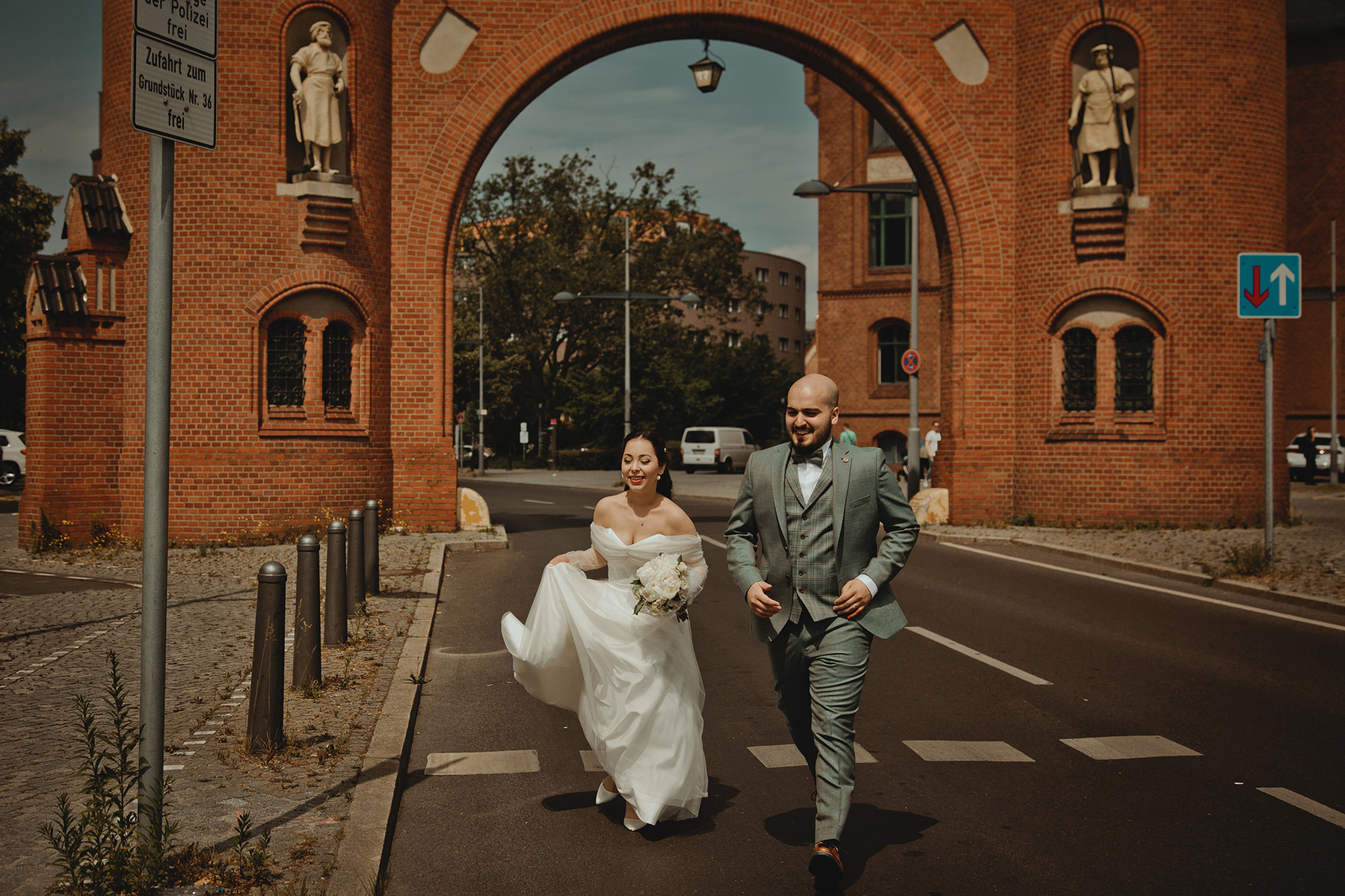 Gülsüm und Mehmet rennen für ihre natürlichen Hochzeitsbilder in Berlin über eine Straße. Im Hintergrund ist das Borsigtor zu sehen.