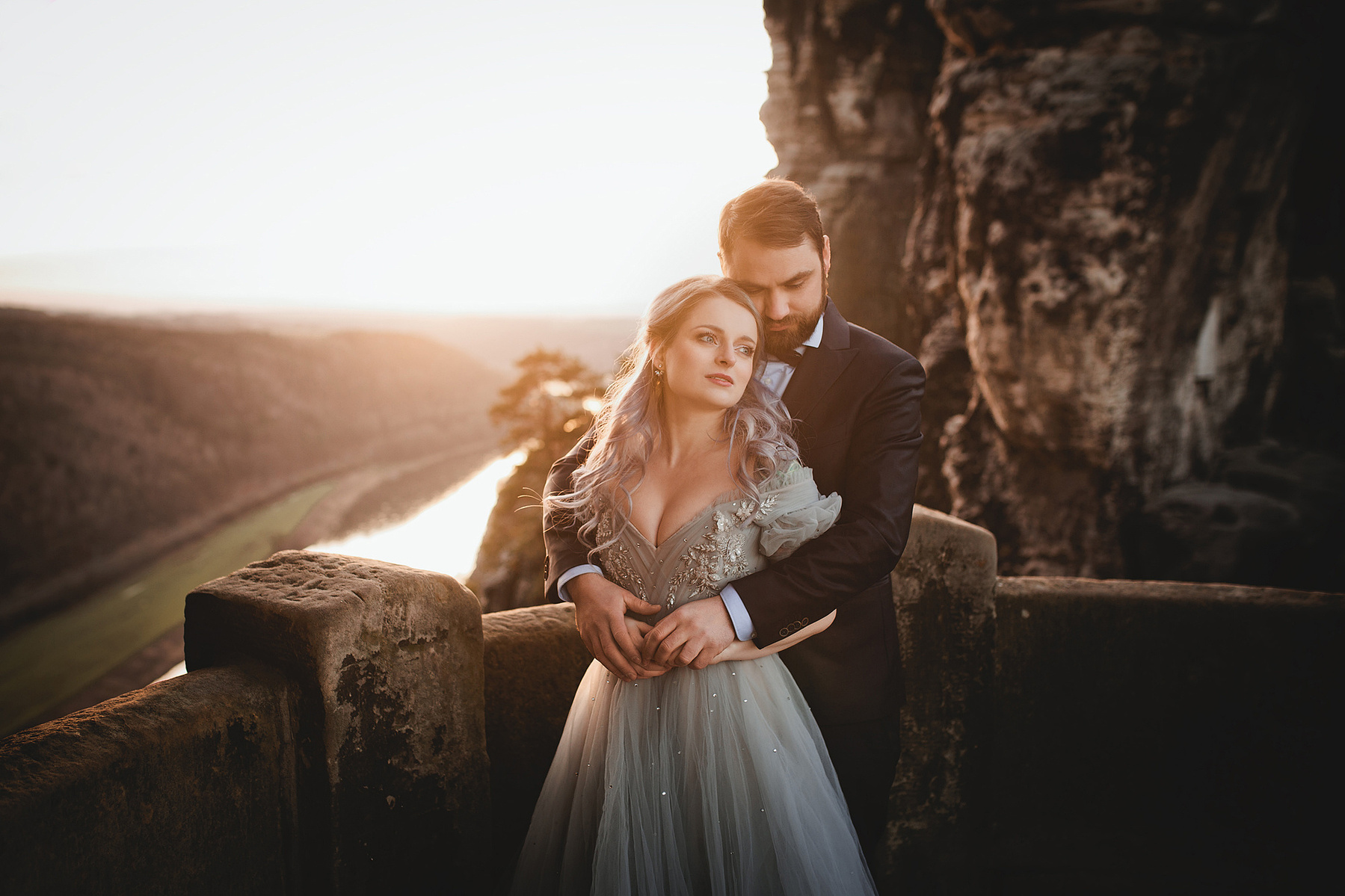 Beim After Wedding Shooting im Elbsandsteingebirge lehnt sich eine Frau im farbigen Hochzeitskleid an ihren Ehemann an.