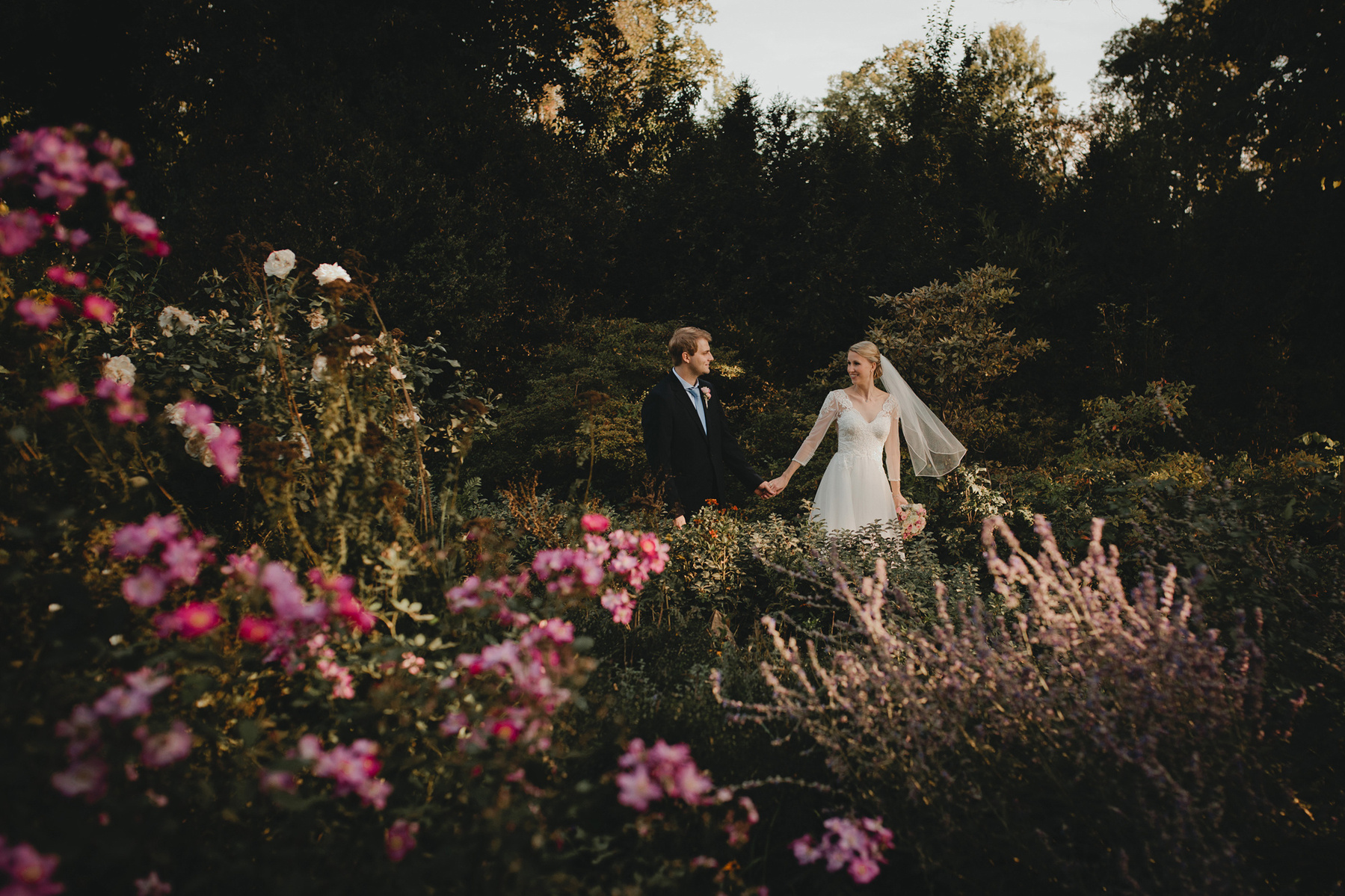 Ein Brautpaar läuft für ungestellte Hochzeitsfotos händchenhaltend durch den blühenden Schlosspark Köpenick.