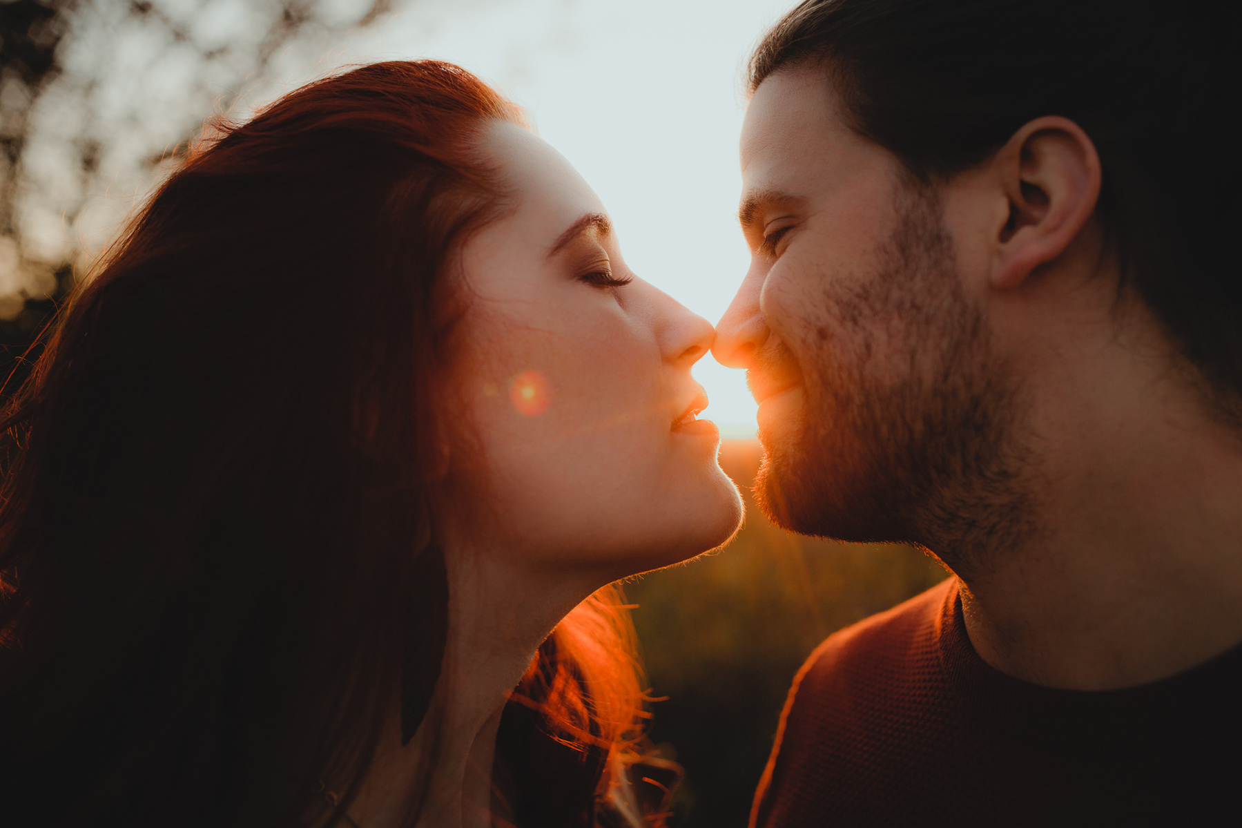 Nahaufnahme eines sich küssenden Paares. Zwischen den sich beinahe berührenden Lippen scheinen die Strahlen der Abendsonne hindurch. 