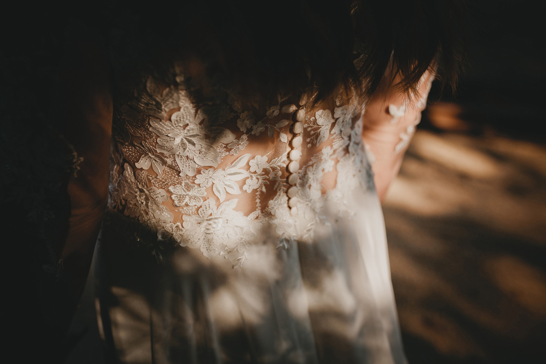 Detailaufnahme eines Brautkleids mit Knopfleiste und Spitze am Rücken. Die Sonne malt ein Schattenspiel auf das Hochzeitskleid.