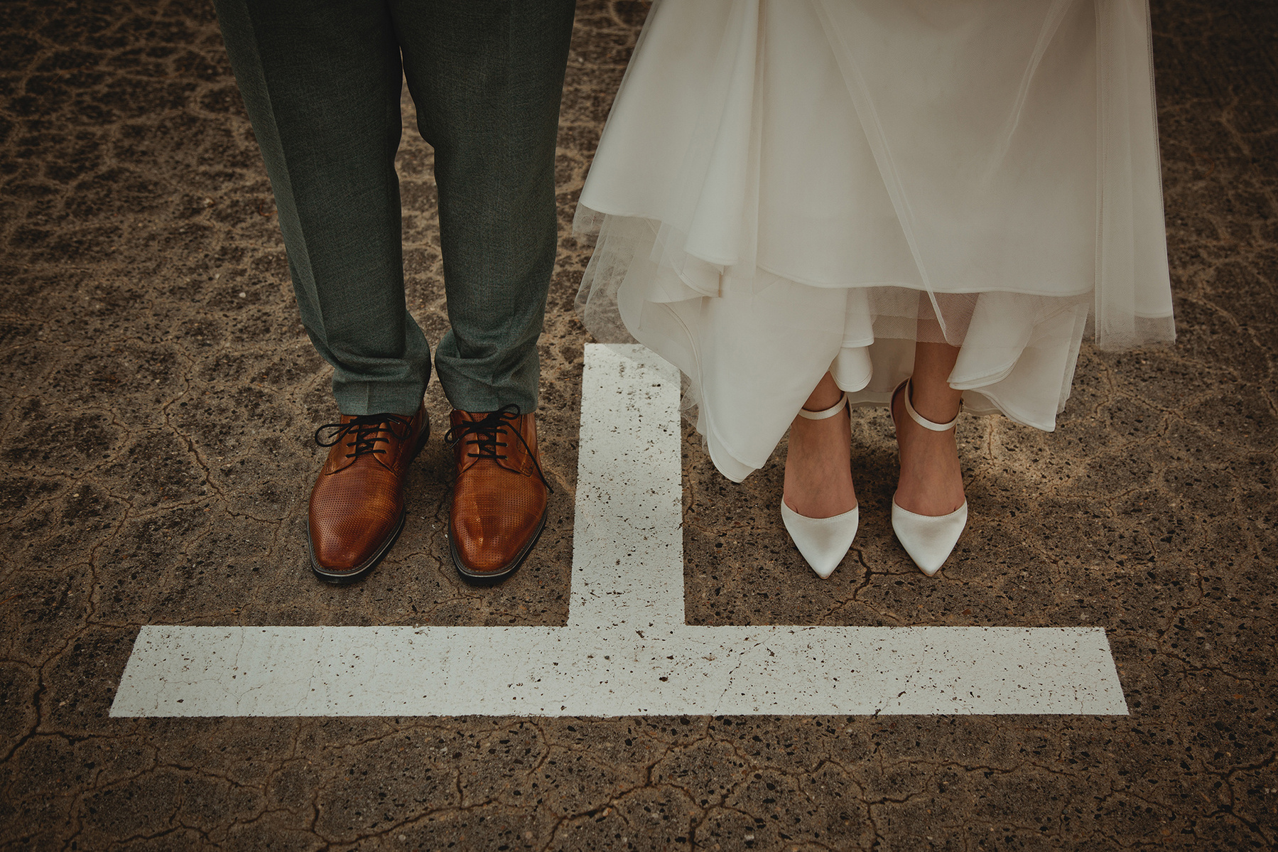 Kreatives Detailfoto einer Hochzeit von den Schuhen des Brautpaars vor der Markierung auf dem Boden in einem Parkhaus.