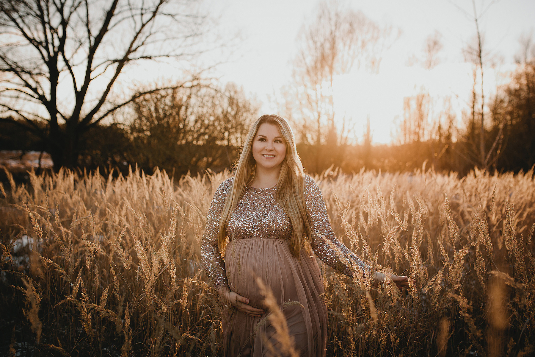 Die werdende Mutter blickt beim outdoor Babybauchshooting strahlend in die Kamera der Familienfotografin aus Berlin.