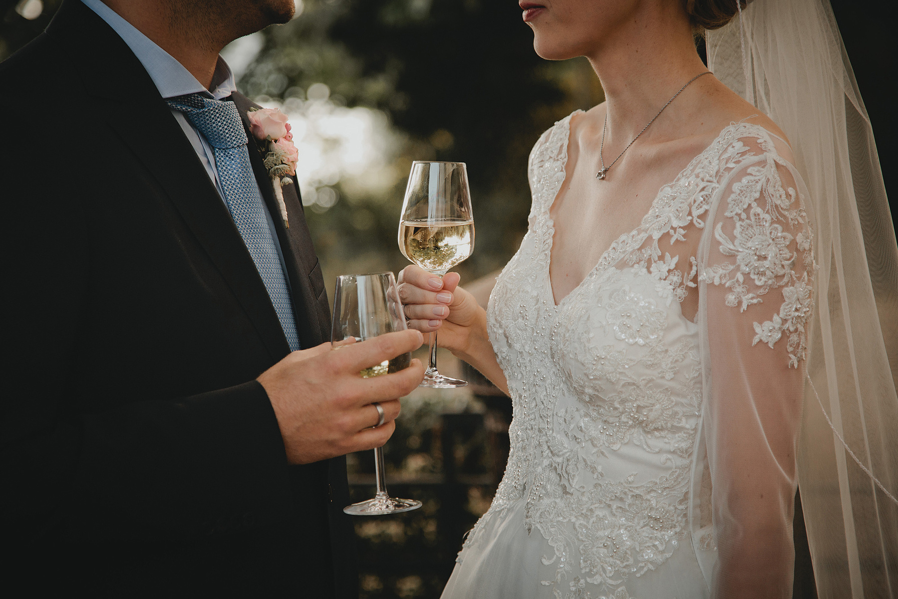 Braut und Bräutigam stoßen bei einer Hochzeit im Grünen mit Sekt an.