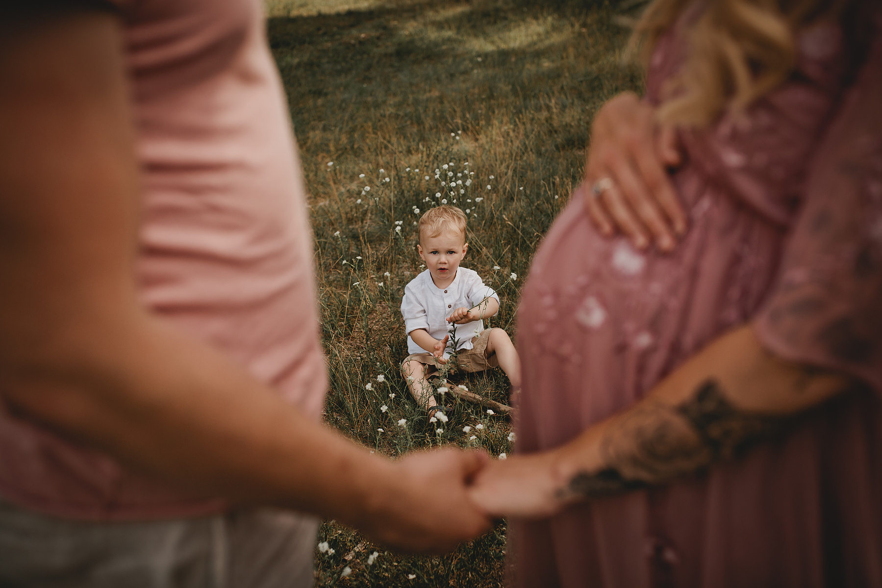 Ein kleiner Junge spielt beim Familienshooting im Gras. Im Vordergund sind seine Eltern zu sehen.