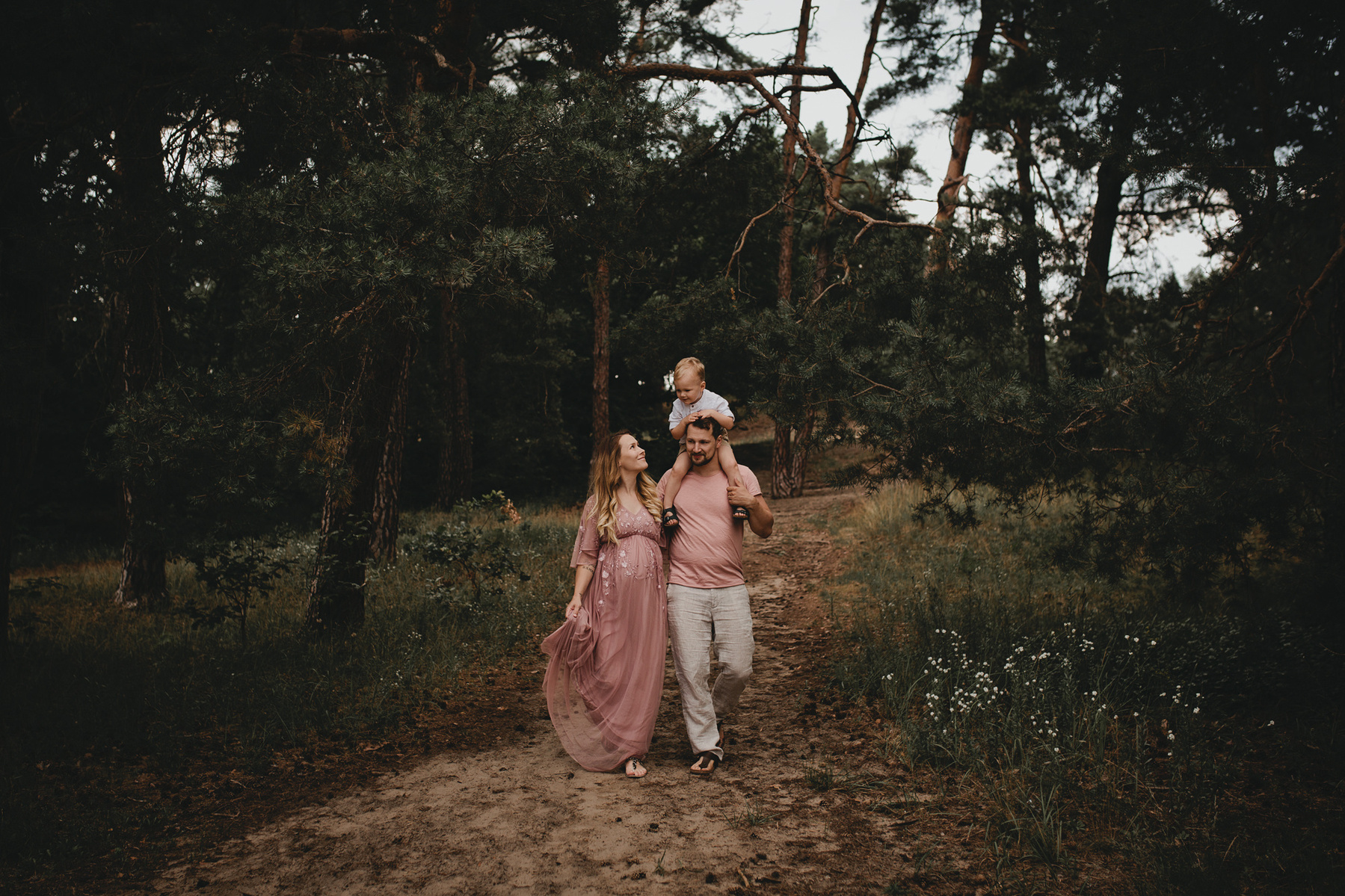 Eine Familie in rosa Outfits läuft beim Fotoshooting durch Kiefernwald in Brandenburg.