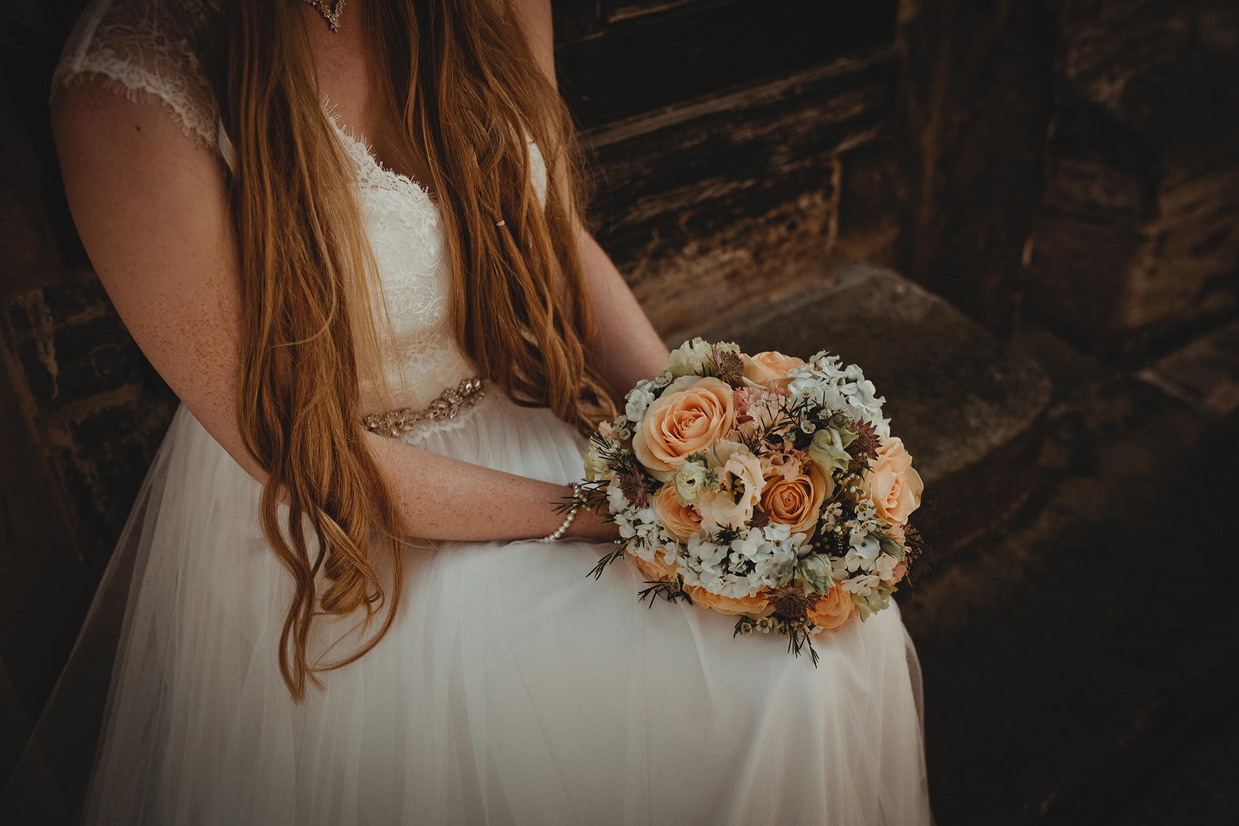 Die Braut trägt ihren Brautstrauß mit Blumen in weiß und apricot. 