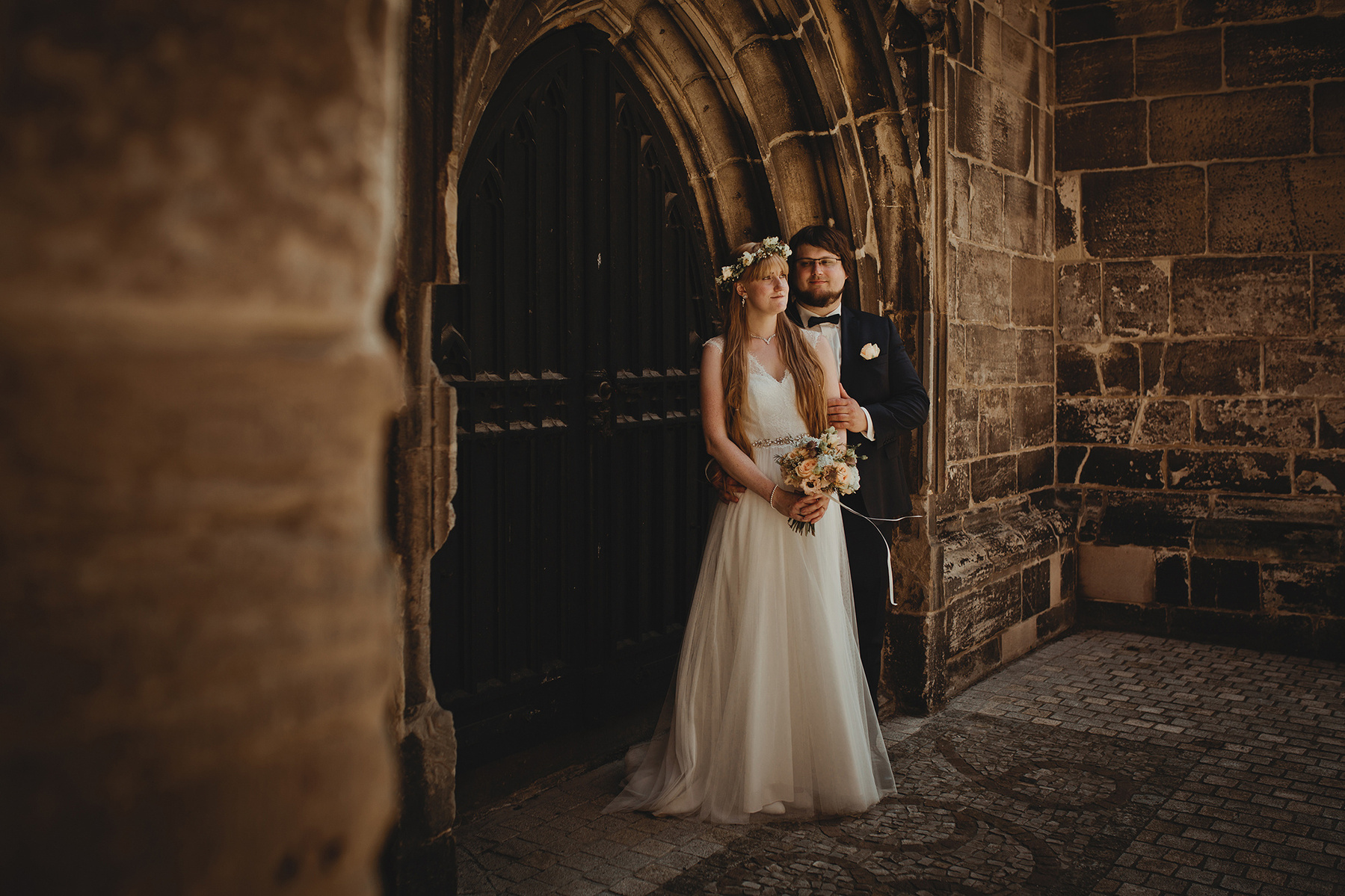 Ein Brautpaar steht für natürliche Hochzeitsfotos in Weißenfels Arm in Arm vor dem Portal der Kirche.