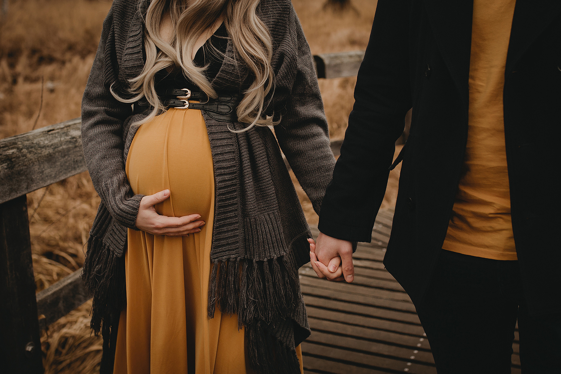 Detailaufnahme vom Schwangerschaftsshooting mit Jessi & Amin. Sie halten einander an der Hand und Jessi streichelt ihren Babybauch.