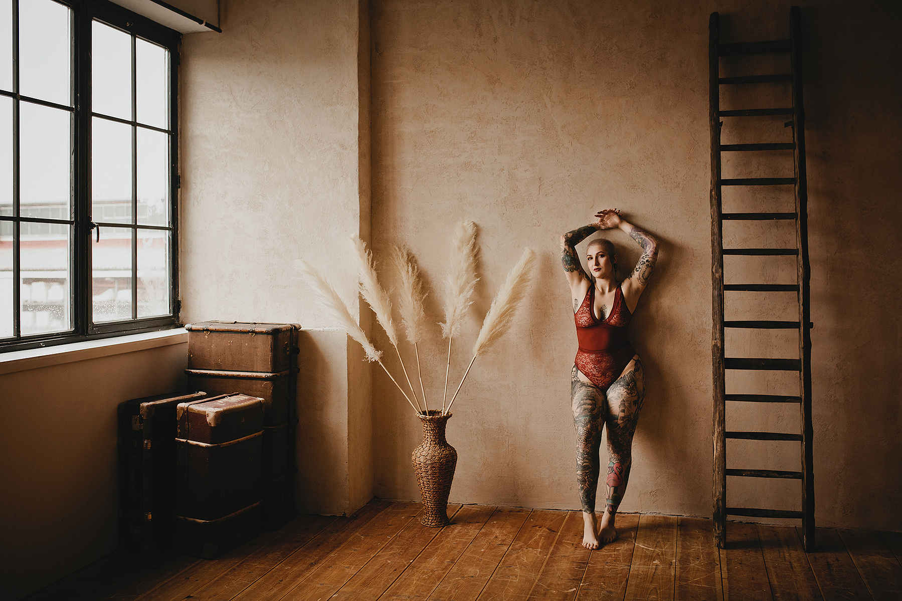 Eine Frau in roten Dessous lehnt beim Boudoirshooting an der Wand eines Loft Fotostudios in Berlin. 