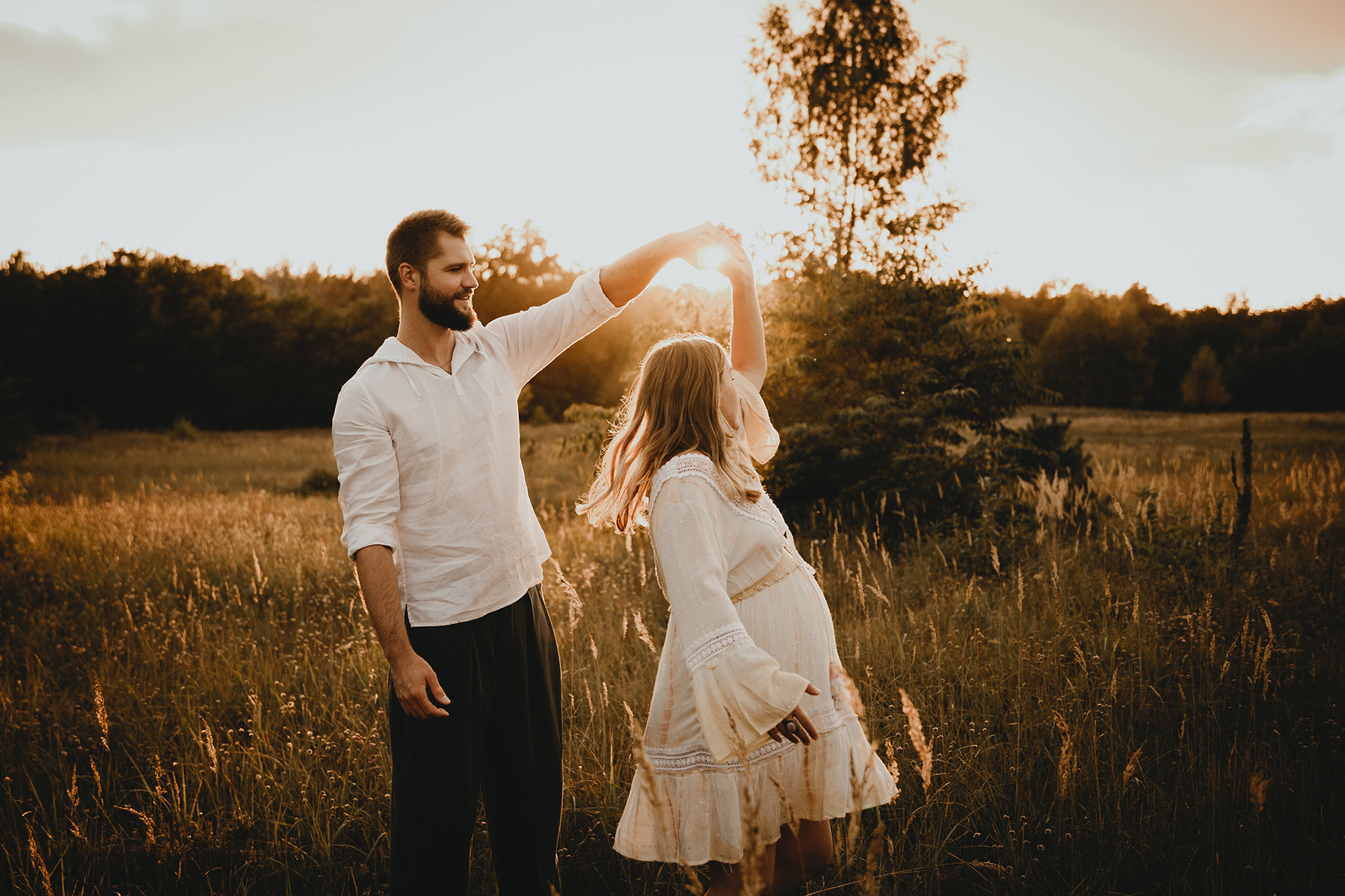 Ein Paar tanzt für natürliche Babybauchfotos in Berlin im Abendlicht auf einer Wiese.