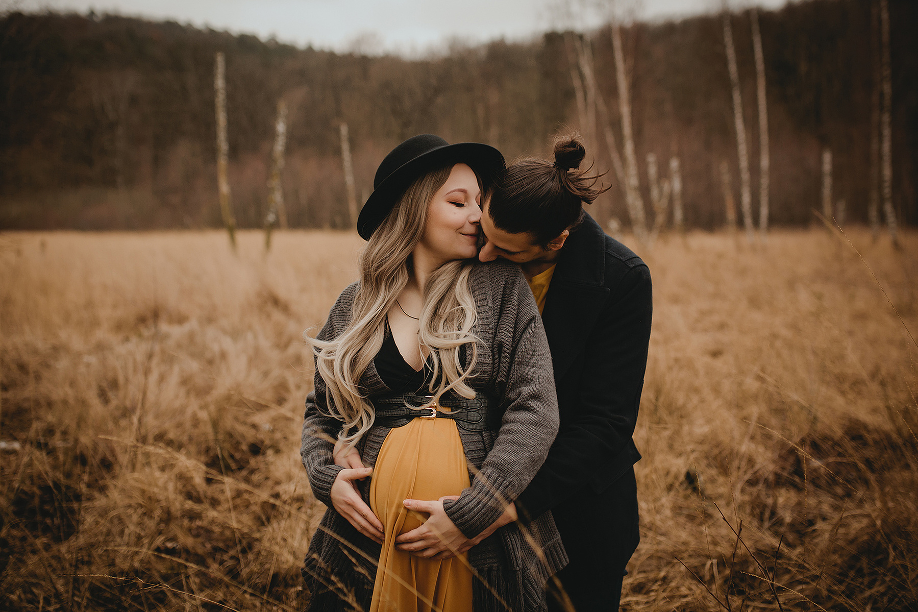 Eine schwangere Frau wird beim Babybauchshooting im Winter von ihrem Mann umarmt und geküsst.