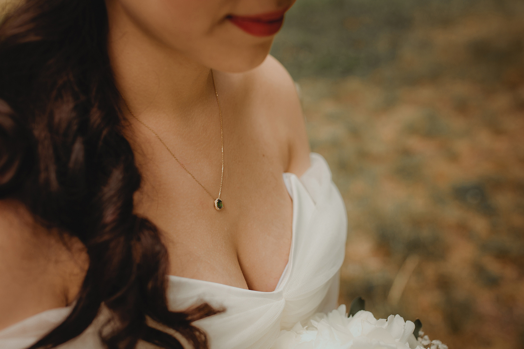 Stimmungsvolle Detailaufnahme vom Brautschmuck. Am Hals der Braut hängt eine zarte goldene Kette mit einem grünen Stein.