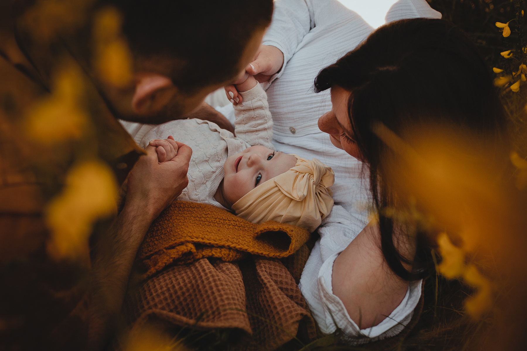 Die Eltern spielen mit ihrer Tochter bei einem natürlichen Familienshooting ganz entspannt auf einer Decke. 