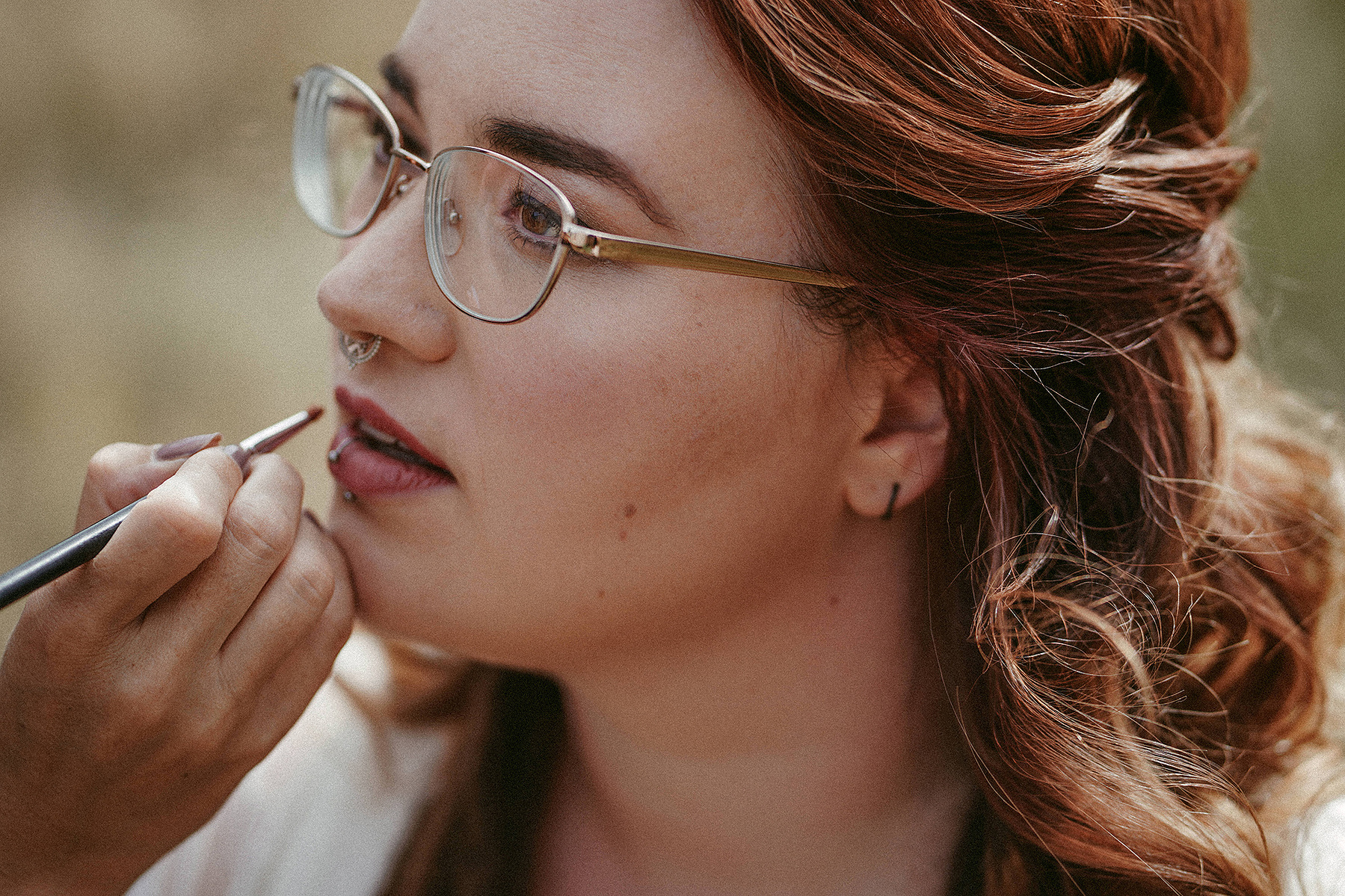 Detailaufnahme vom Brautstyling am Hochzeitsmorgen. Einer Braut mit Brille werden die Lippen geschminkt.