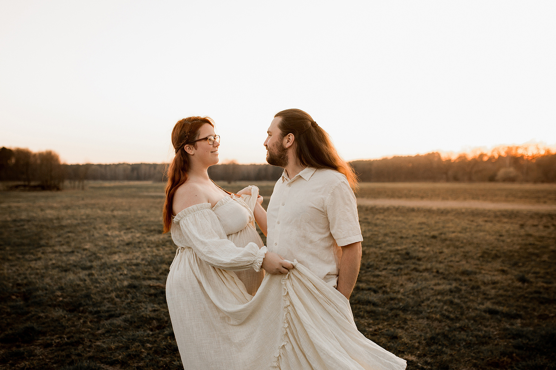 Auf einer weiten Wiese tanzt ein Pärchen beim Fotoshooting im Abendlicht. 