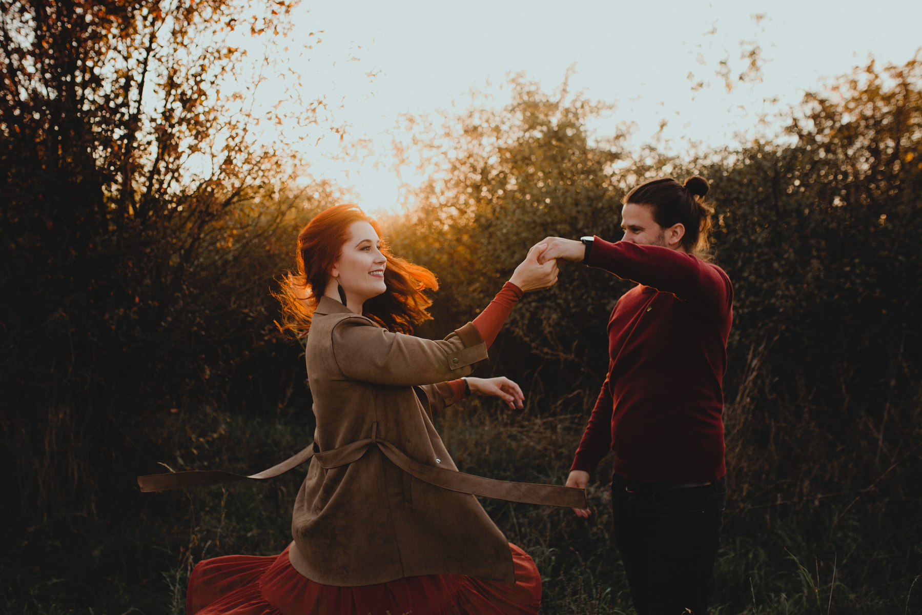 Ein Pärchen in herbstlichen Outfits tanzt beim Couple Shoot im Abendlicht. Ihre roten Haare leuchten in der untergehenden Sonne.