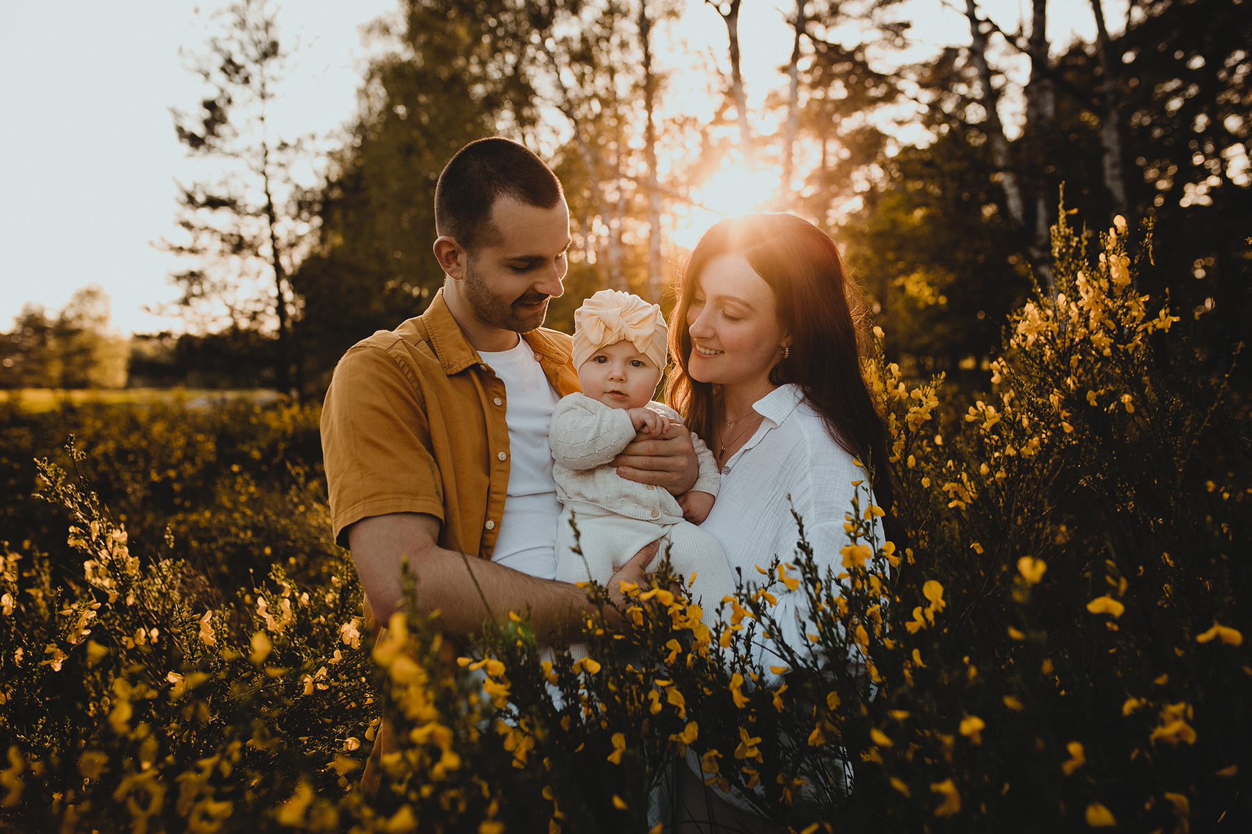 Mit ihrer Tochter auf dem Arm posieren die Eltern beim Fotoshooting im Sonnenuntergang für die Kamera der Familienfotografin aus Berlin. 