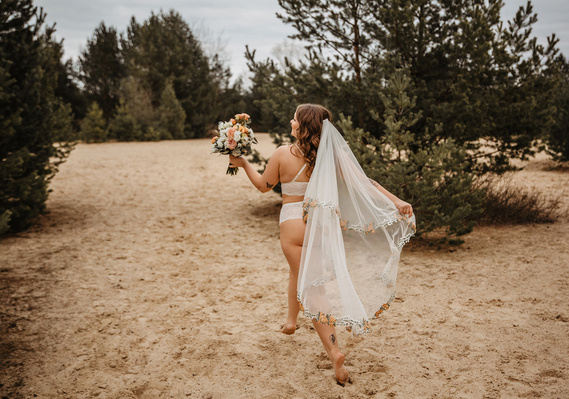 Eine Braut läuft beim Boudoir Fotoshooting in Berlin mit wehendem Schleier über eine Sanddüne. 