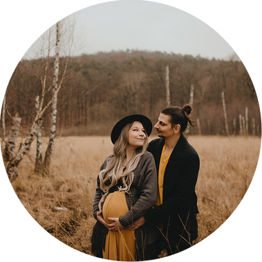 Ein Mann und seine schwangere Frau stehen beim Babybauchshooting Arm in Arm vor einer Moorwiese und schaut einander lächelnd in die Augen. 