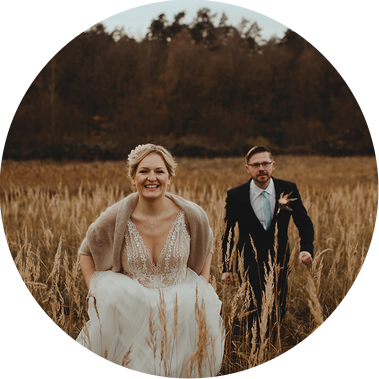 Ein Brautpaar rennt beim Fotoshooting nach der Hochzeit lachend über ein Feld. 