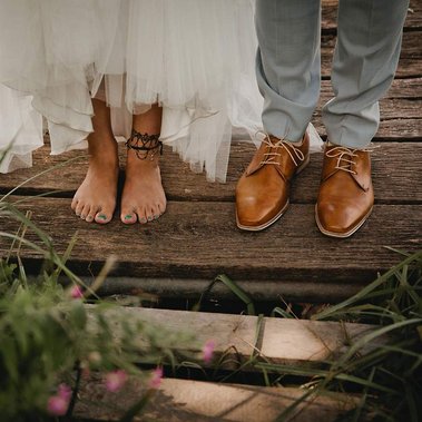 Detailaufnahme einer unkonventionellen Hippie Hochzeit im Landgut Stober. Die Braut ist barfuß und der Bräutigam trägt braune Schuhe.