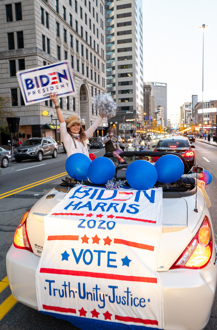 A girl holding Biden sign during the celebration of Biden victory in the 2020 United States presidential election, a white car decorated with Biden Harris sign and blue balloons