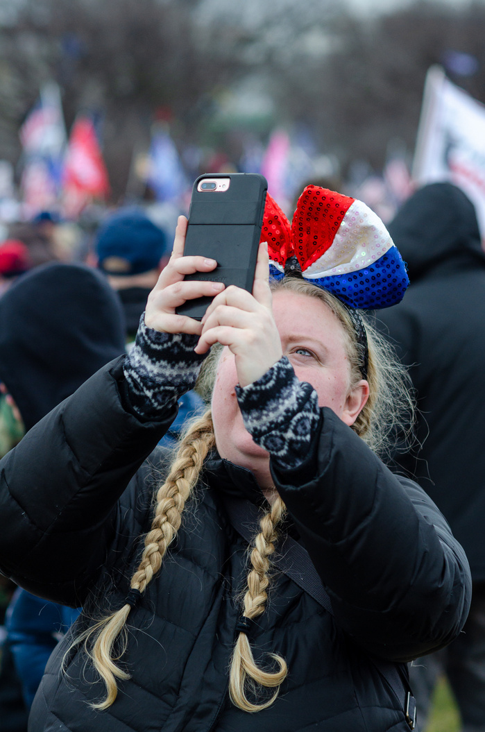 A blond girl with braids wearing patriotic bow taking selfie at a pro-Trump rally