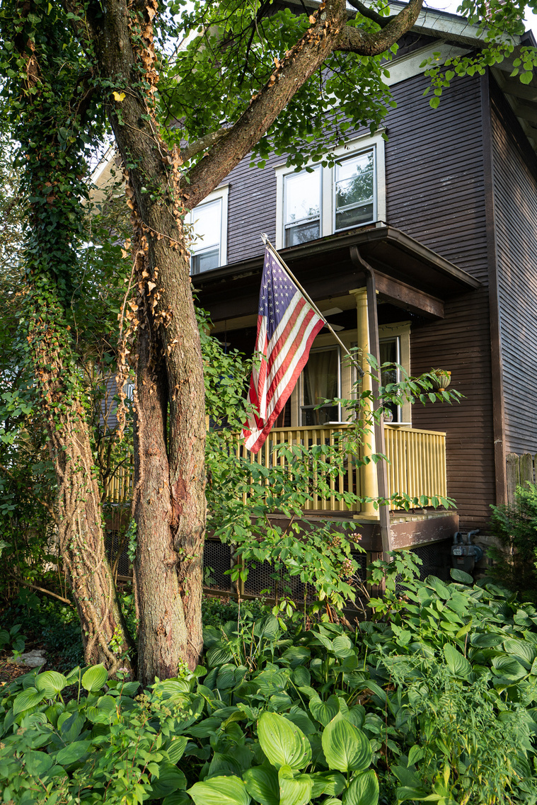 An Old American flag hanging on a porch of an old house, surrounded by old tree and green plants, before the 2020 United States presidential election